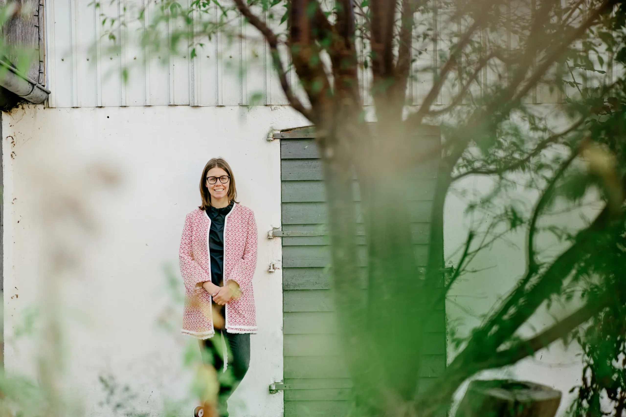 Portræt af advokat i fuld figur, der læner sig op ad en hvid bygning med grønne planter i forgrunden.